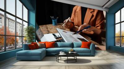 Two businesswomen pointing at financial charts and graphs on a report with a pen while working late in the office Wall mural