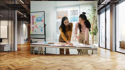 Two female uiux designers are discussing over mobile app interface wireframe design prototypes on table at modern office Wall mural