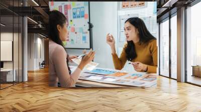 Two female uiux designers discussing over mobile app interface wireframe design in office Wall mural