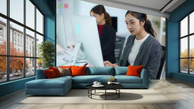 Young asian businesswoman concentrating and typing on a computer keyboard while working in a modern office Wall mural