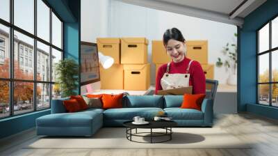 Young woman managing her online store, checking orders and preparing packages for shipment Wall mural