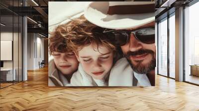 A close-up shot of a man in a hat and sunglasses with two boys, all resting on a sunny beach. The image captures a moment of togetherness, relaxation, and familial love. Wall mural