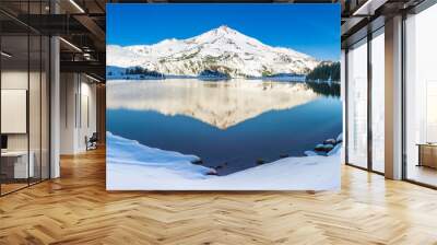 A snow covered mountain peak is reflected in the calm morning waters of a high elevation lake. Wall mural