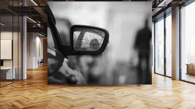 Black-and-white sad image of the rearview mirror of a light car, strewn with raindrops and the black silhouette of a passing man. Wall mural