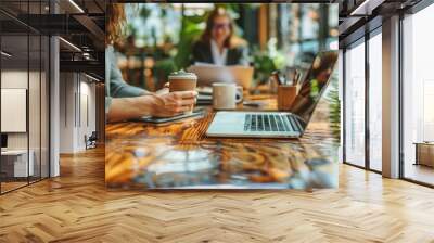 Two individuals are engaged in their work at a cafe, with laptops and coffee, a scene blending business with a casual setting. Wall mural