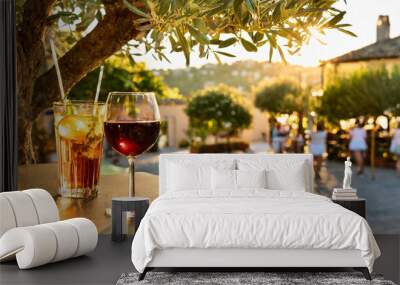 Verre de vin et cocktail à la terrasse d'un bar restaurant pendant les vacances d'été dans un joli village à profiter d'une journée ensoleillée de détente à l'ombre d'un olivier Wall mural