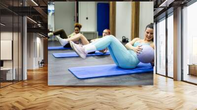 A group of 3 young women of different ethnicities are performing an abs class lying on the floor with the help of a small ball. Concept of abs classes. Take out the six-pack Wall mural