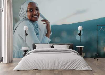 African Muslim woman in the night on a balcony smiling at the camera with city bokeh lights in the background. Wall mural