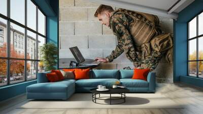 American soldier in military uniform using laptop computer for drone controlling and to stay in contact with friends and family Wall mural