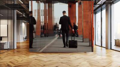 Going to airport terminal. Confident businessman traveler walking on city streets and pulling his suitcase drinking coffee and speaking on smartphone Wall mural