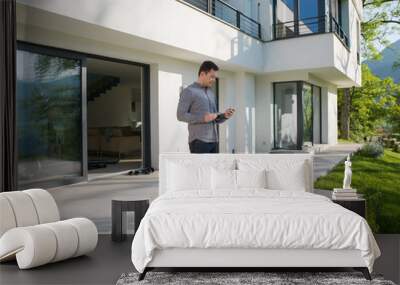 man using mobile phone in front of his luxury home villa Wall mural