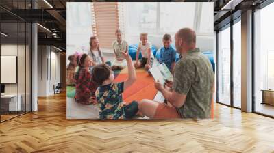 Reading time in elementary school or kindergarten, teacher reading a book to kids in elementary school or kindergaden. Selective focus  Wall mural