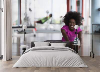 woman in a gym stretching and warming up man in background working with dumbbels Wall mural