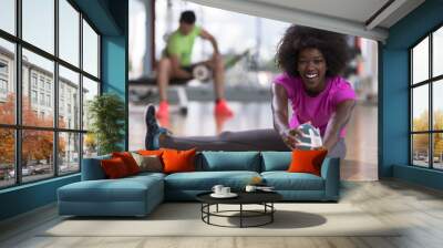 woman in a gym stretching and warming up man in background working with dumbbels Wall mural