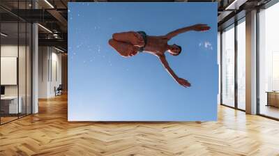 Young teen boy jumping flying and diving in the river. Clear blue sky and trees in distance as a natural background. Wall mural