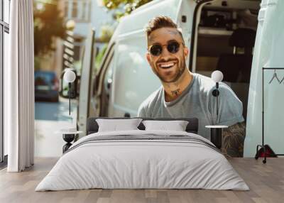 portrait of a handsome and stylish man in tattoos and black glasses next to a car Wall mural