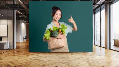 Asian girl portrait holding a bag of vegetables on a green background Wall mural