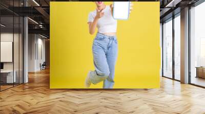 full body image of young Asian girl holding phone with cheerful face on yellow background Wall mural