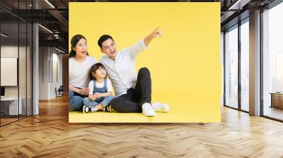 Image of Asian family sitting together happy and isolated on yellow background Wall mural