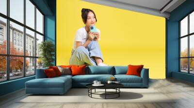 portrait of a beautiful young asian girl sitting on a yellow background Wall mural