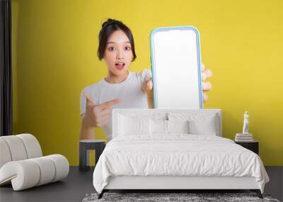 Young Asian woman holding phone with cheerful face on yellow background Wall mural