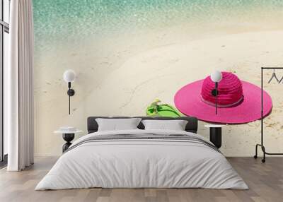 Pink beach hat and green slippers in the golden sand by sea shor Wall mural