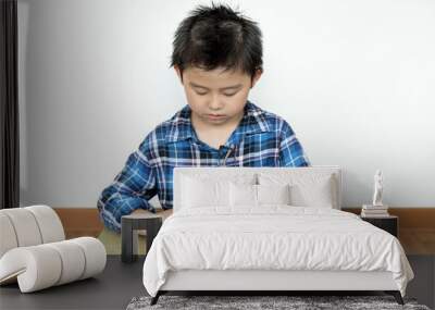 Little student boy without glasses doing his homework on the table with white background Wall mural