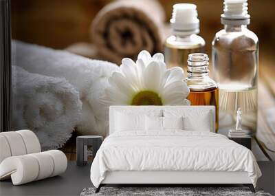 A serene spa setting with two glass bottles of essential oils, one large and the other small, lying on top of neatly folded white towels on a bamboo mat. A single daisy flower lies beside them Wall mural