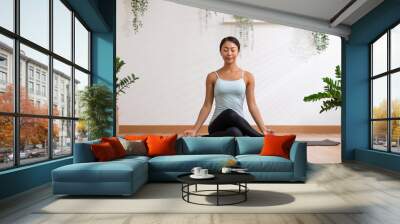 Calm of wellness Asian young woman sit on yoga mat doing breathing with yoga lotus pose.Yoga meditation of young healthy woman relax and comfortable at white cozy home,Yoga Exercise Wellness Concept Wall mural