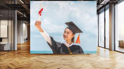 Graduated woman in cap and gown holding certificated celebrating in Commencement day with blue sky on the beach with beautiful sea in summer so proud and happiness,Education Success in summer Concept Wall mural