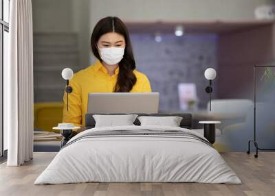 New normal of Asian woman in yellow shirt wearing surgical face mask working with computer laptop thinking to get ideas and requirement in Business startup at modern office or Co-working space Wall mural