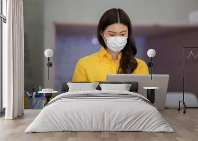 New normal of Asian woman in yellow shirt wearing surgical face mask working with computer laptop thinking to get ideas and requirement in Business startup at modern office or Co-working space Wall mural