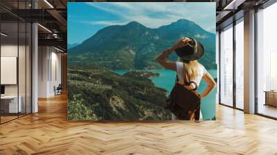 Back view of wanderlust woman with backpack looking at scenic view of lake and mountains from a view point. Wall mural