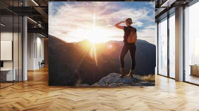 Young blonde woman with backpack standing on the peak of mountain looking far away.  Alps scenery. Traveler concept. Wall mural