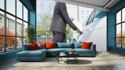 Businessman plugging in the charger in electric car and going to work in business center - skyscraper Wall mural