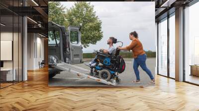 Female assistant transferring a man with disability into the vehicle by pushing his wheelchair up the accessible car ramp. Wall mural