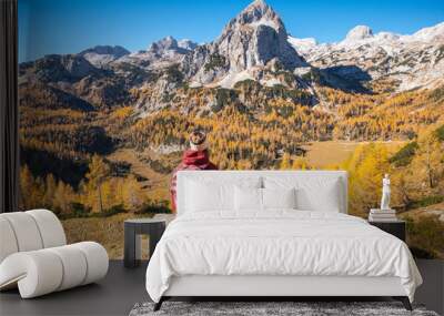 Female hiker on a bench enjoying mountain panorama view on a sunny autumn day with golden larch trees. Wall mural