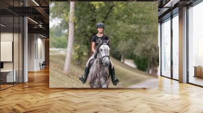 Female rider, horseback riding along the trail that leads between white wood fences and fields. Equestrian leisure activity concept. Wall mural