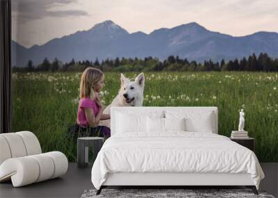 Girl child playing with their pet dog on a spring meadow at sunset with mountains in the background. Wall mural