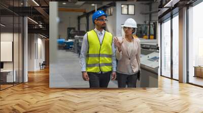 Indian female factory manager introducing the production line to a recruit, an African American worker, and congratulating him on a new job, front view. Wall mural