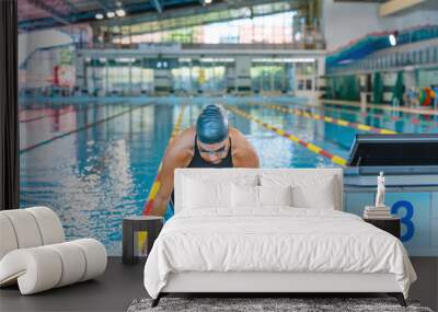 Portrait of a woman, a professional swimmer in black one-piece swimwear and a black cap with goggles Wall mural