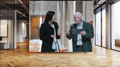 Senior vintner guiding a female visitor through his winery, explaining the process and equipment in wine industry at production cellar by using tablet Wall mural