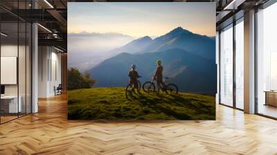 Two females on mountain bikes talking and looking at beautiful sunset Wall mural