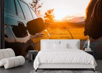 Young woman plugging in the charger in a black electric car, renewable energy concept Wall mural