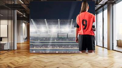 female soccer player standing with the ball against the crowded stadium at night Wall mural