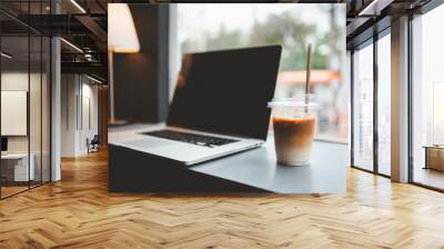 A glass of iced coffee on the table with blurred laptop background in cafe. Wall mural