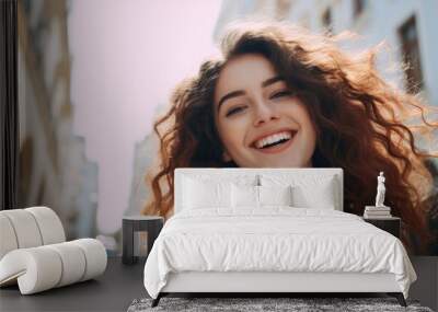 A woman with layered curly hair is laughing and smiling as she strolls down a bustling city street, clearly enjoying the vibrant atmosphere and having fun during her travel adventure Wall mural