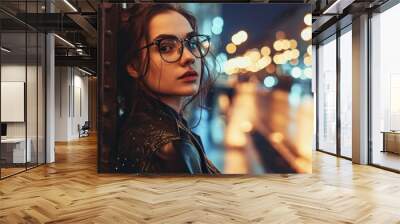 Fashionable brunette girl in trendy clothes and glasses enjoying city nightlife. Beautiful hipster in a leather jacket outside with street lights. Wall mural