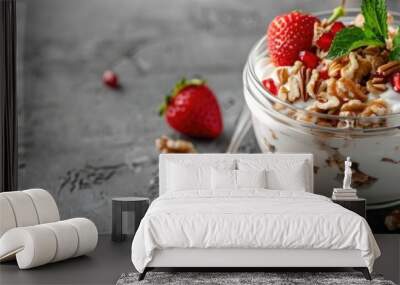 Greek yogurt topped with nuts and strawberries in a glass jar on a textured surface, paired with a spoon. Close-up perspective allowing for text placement. A wholesome breakfast highlighting fresh Wall mural