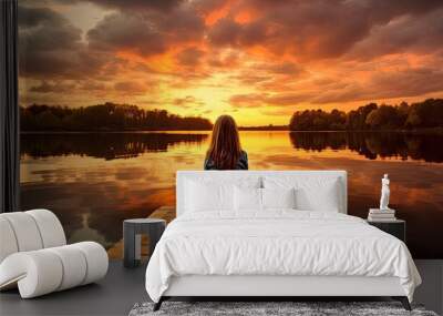 Little girl on pier watching sunset, reflected in lake. Wall mural